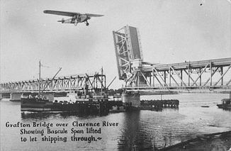 Grafton Bridge über den Clarence River. Eine Sektion ist geöffnet, um den Schiffsverkehr durchzulassen. (Postkarte von ca. 1932; Das Southern-Cross-Flugzeug wurde nachträglich zum Foto hinzugefügt.)