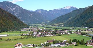 Blick von Kirchdorf i.T. nordostwärts über das Großachental und Erpfendorf in die Wald und den Griesbachunterlauf (hinten, Oberlauf hinter dem zweiten Bergfuß rechts), fern Fellhorn und Steinplatte