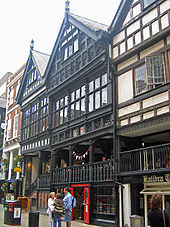 Das Bild zeigt ein Haus mit Holzfassade und einer rtgestrichenen Doppeltüre im Erdgeschoss