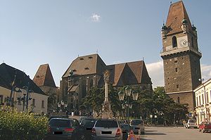 Der Turm rechts weist einen auskragenden Wehrgang auf, im Zentrum die Pfarrkirche